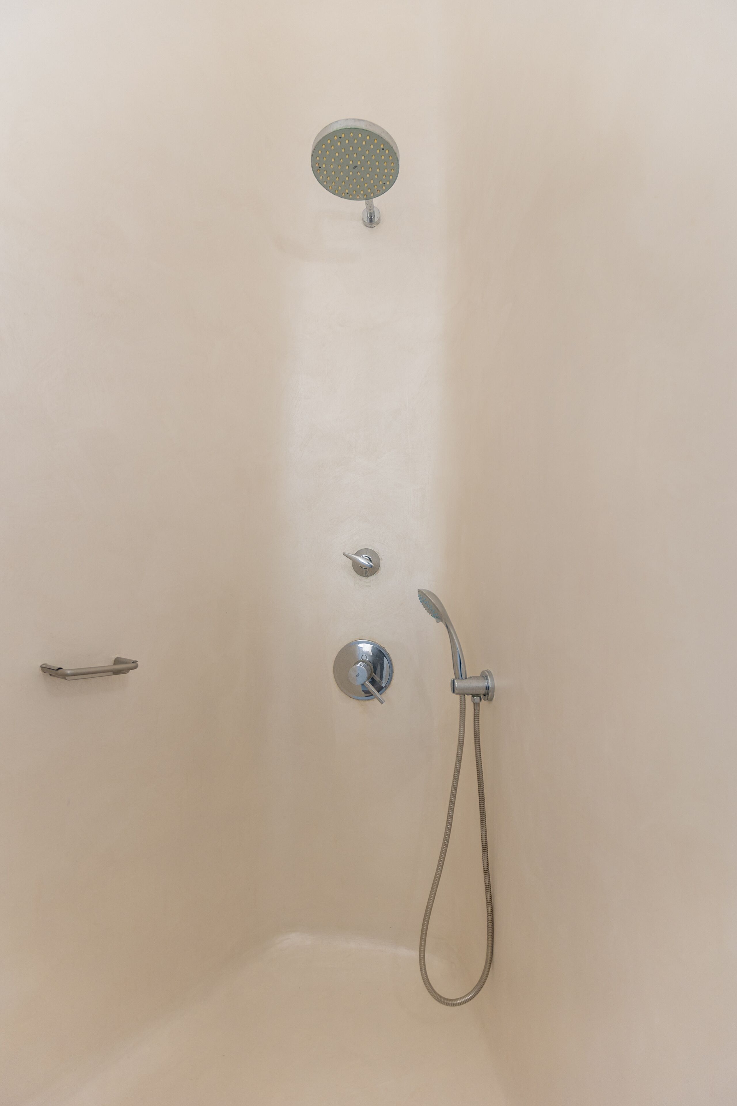 A shower with a handheld showerhead and a wall-mounted control panel.