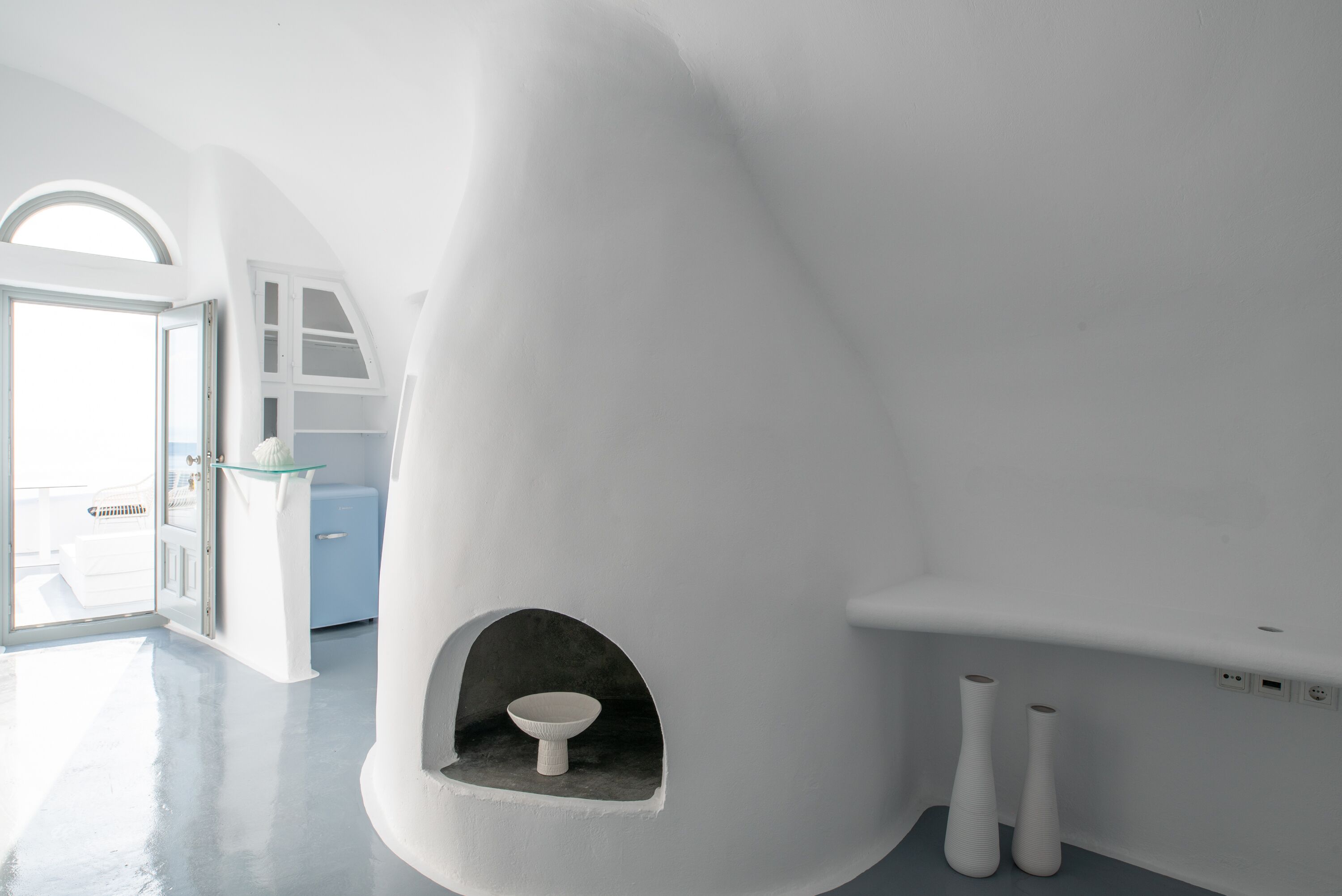 Een moderne, minimalistische badkamer met een uniek architectonisch ontwerp, met een gebogen wastafel en een klein nisje met een zuilenvormig wasbakje.