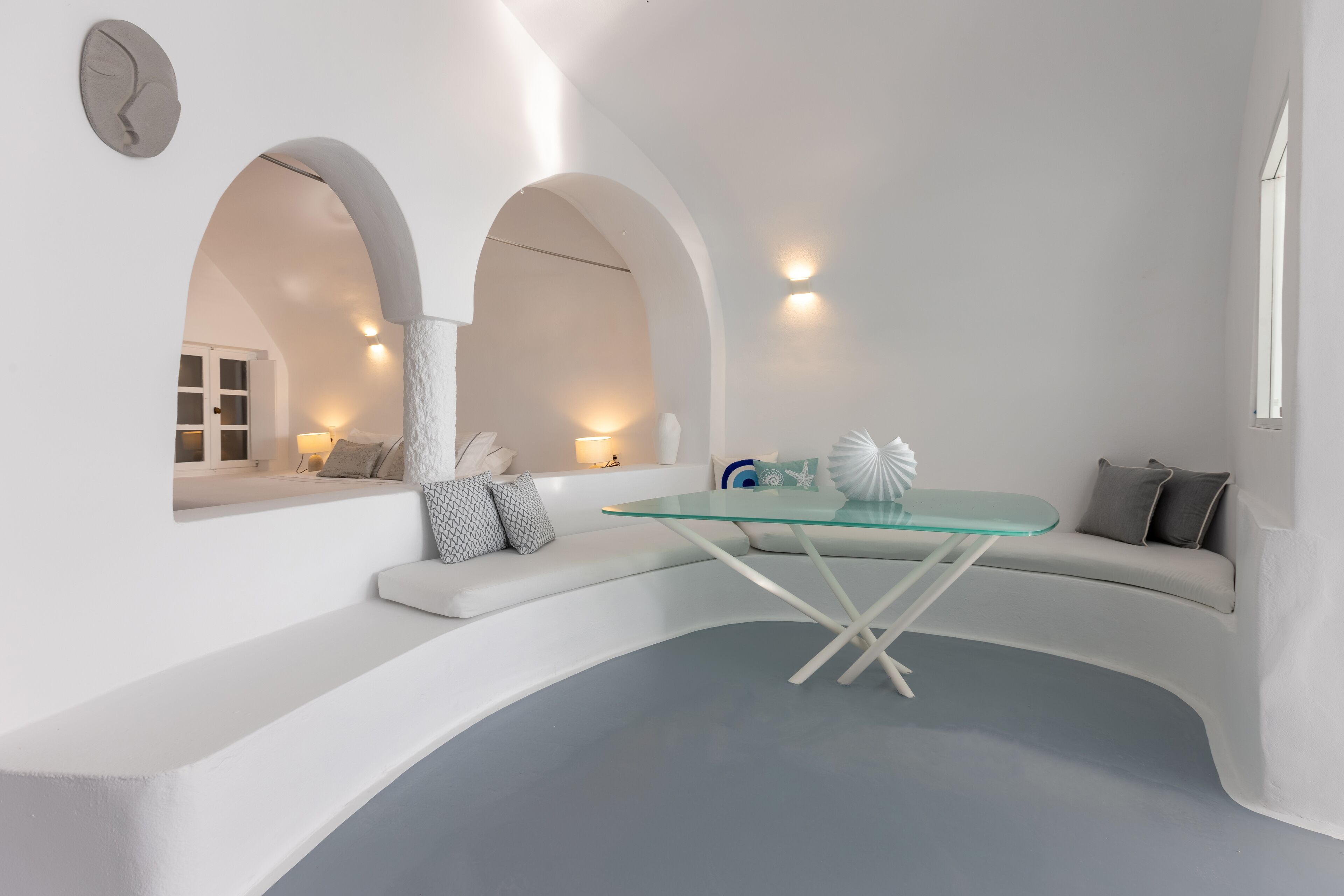 Um interior moderno com mesa de vidro curva, sofás brancos e nichos em arco.