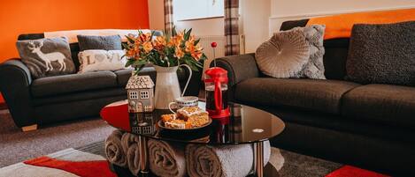A living room with a sofa, a coffee table with a vase of flowers, and a tray with cookies.