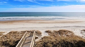 A wooden boardwalk leading to a sandy beach with the ocean in the background.