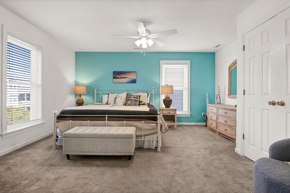 A bedroom with a bed, a nightstand, a dresser, a ceiling fan, and a window with blinds. - Seahorse Sanctuary - A breathtaking ocean front home - 4 bedroom (North Topsail Beach)