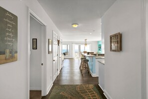 A hallway with a view to the ocean, a kitchen with a bar, and a dining area with stools.