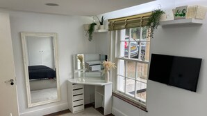 A bedroom with a bed, a desk with a mirror, a TV mounted on the wall, and a window with blinds. - Lovely 2-bed Apartment in Brixton Central Location (London)