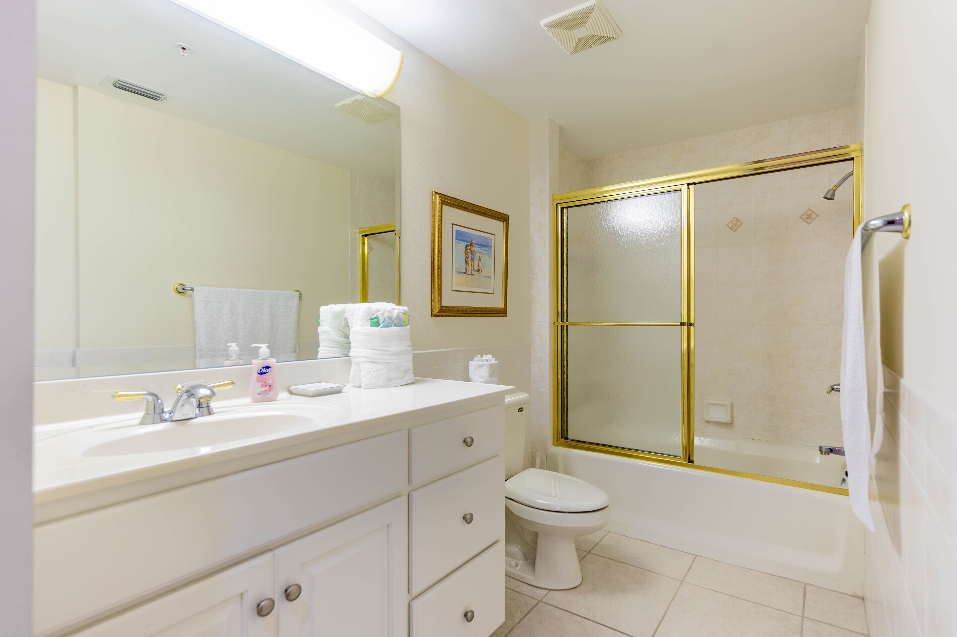 A bathroom with a white sink, toilet, and shower with gold trim.