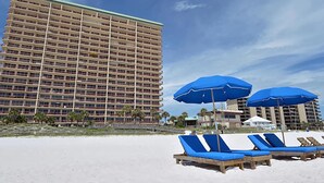 A beachfront hotel with multiple floors, a sandy beach in the foreground, and blue umbrellas providing shade. - Hidden Dunes 11th Flr 3BR 3BA Slps 12!! (Panama City Beach)