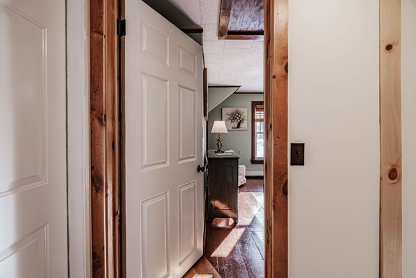 A hallway with a white door, wooden beams, and a lamp on a table. - Adventure Trails Farm in Bethel Maine (Bethel)