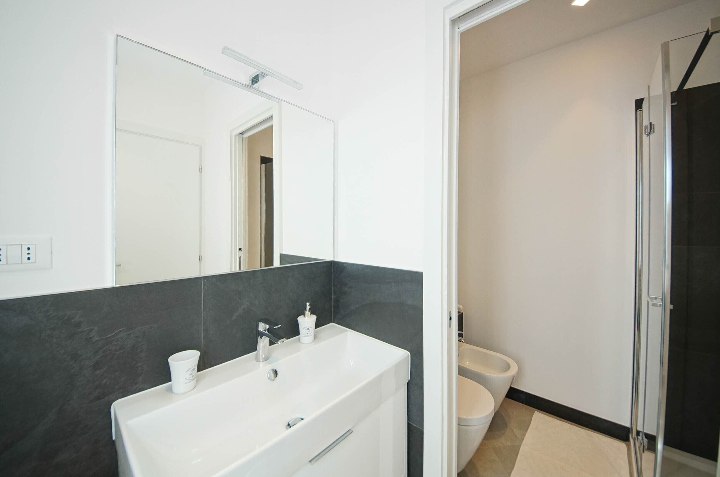A modern bathroom with a white sink, mirror, and dark tiled walls.
