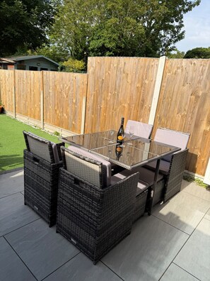 An outdoor patio with a glass-top table, wicker chairs, and a bottle of wine. - The Seaside Haven w/ Parking - Mins to Viking Bay - EV Charger (Broadstairs)