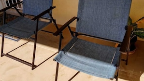 To blå vævede stole med metalstel på en fliseterrasse.