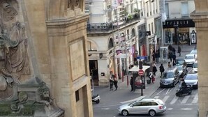 An ornate stone archway with classical carvings, a bustling street with pedestrians and vehicles, and pigeons on the ground. - Hotel Allety (Paris)