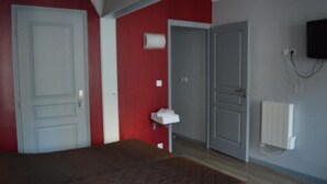 A room with a bed, a white door, a red wall, a gray door, a white radiator, and a TV mounted on the wall. - Hotel Allety (Paris)