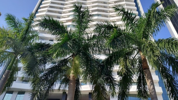 A tall, modern building with a white facade and multiple balconies. Palm trees are in the foreground. - Mondial Apartments By BnbHost (Salvador)