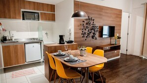 A modern kitchen with a microwave, refrigerator, and dining area with yellow chairs and a wooden table. - Mondial Apartments By BnbHost (Salvador)