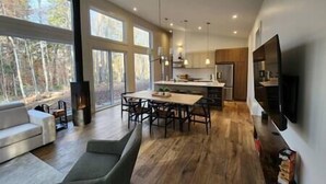 A modern kitchen with a central island, large windows, and a built-in TV. - EARTH chalet in harmony with nature, Tremblant (Mont-Tremblant)