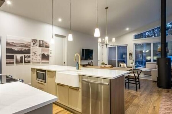 A modern kitchen with a central island, pendant lighting, and a large window. - EARTH chalet in harmony with nature, Tremblant (Mont-Tremblant)