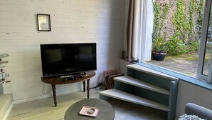 Una sala de estar moderna con un televisor de pantalla plana, una mesita redonda con una taza, dos sofás grises, una escalera que lleva a un balcón y un reloj en la pared.