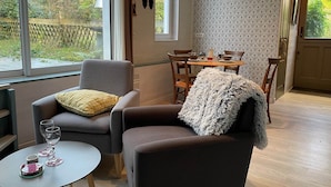 Una sala de estar moderna con un sillón gris, una mesita redonda con copas de vino y un comedor con una mesa de madera y sillas.