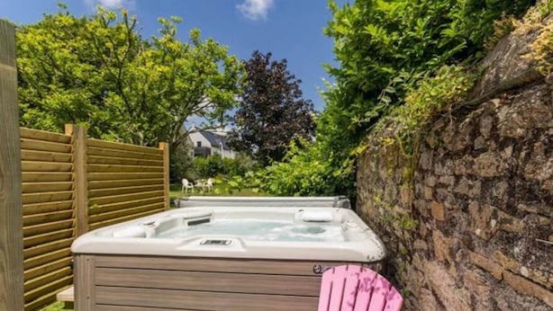 Un jacuzzi en un patio trasero con un cerco de madera, un muro de ladrillo y una silla rosa.