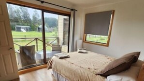 Une chambre dotée d’une grande porte-fenêtre coulissante donnant sur un balcon, d’un lit à baldaquin et d’une petite table de chevet.