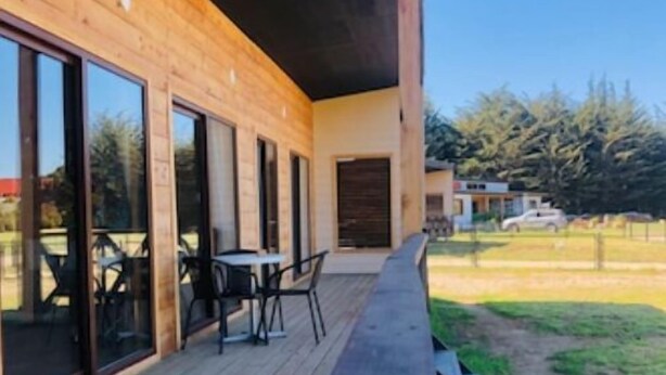 Un bâtiment moderne en bois, doté de grandes portes coulissantes en verre, d’une terrasse avec des meubles d’extérieur et d’une pelouse.