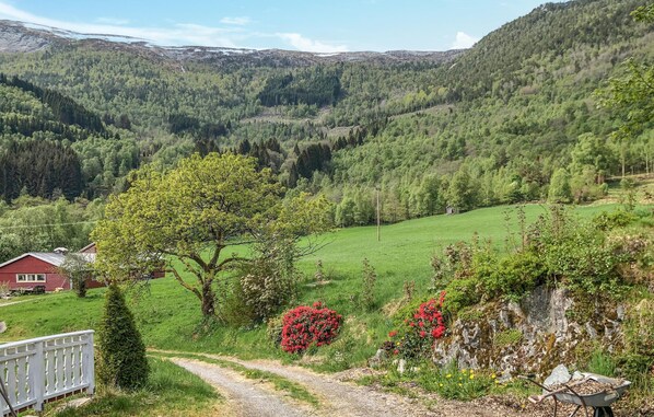 Un paysage rural avec une maison rouge, un chemin de terre et une vallée bordée de forêts denses.