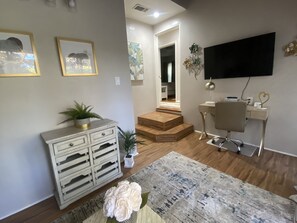 A living room with a sofa, a coffee table, a TV mounted on the wall, a desk with a chair, and a staircase leading to another room. - Stunning Home With Large Yard in Los Angeles (North Hollywood)