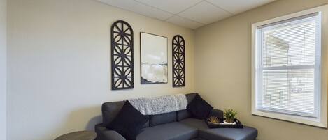 A living room with a grey sectional sofa, a small round table, and decorative wall art.