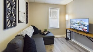Un salon moderne avec un canapé d’angle gris, une table basse en bois et un téléviseur à écran plat posé sur un meuble.