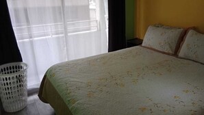 A bedroom with a bed, a window with sheer curtains, a white basket, and a yellow wall. - Apart Latitud (Santiago)