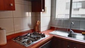 A kitchen with a gas stove, a sink, and a window with a view of buildings. - Apart Latitud (Santiago)