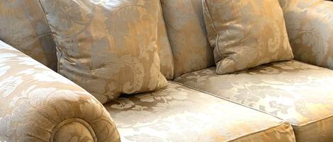 A beige upholstered sofa with a floral pattern, featuring a tufted armrest and three cushions.