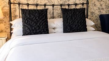 Una cama con cabecera negra y ropa de cama blanca, sobre un fondo de papel tapiz floral.