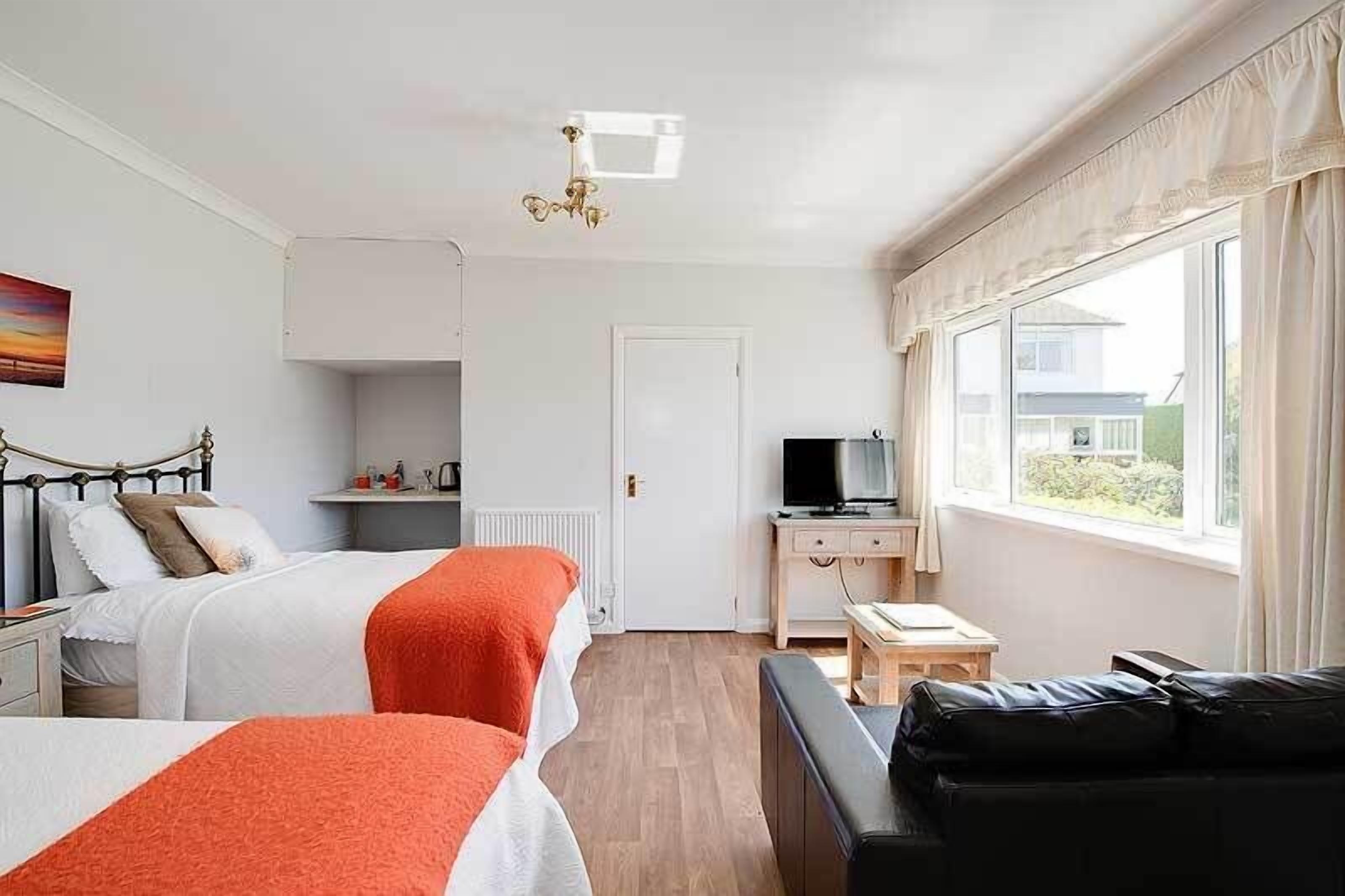 Quarto de hotel com duas camas, uma escrivaninha com televisão, janela com cortinas e vista para o exterior.