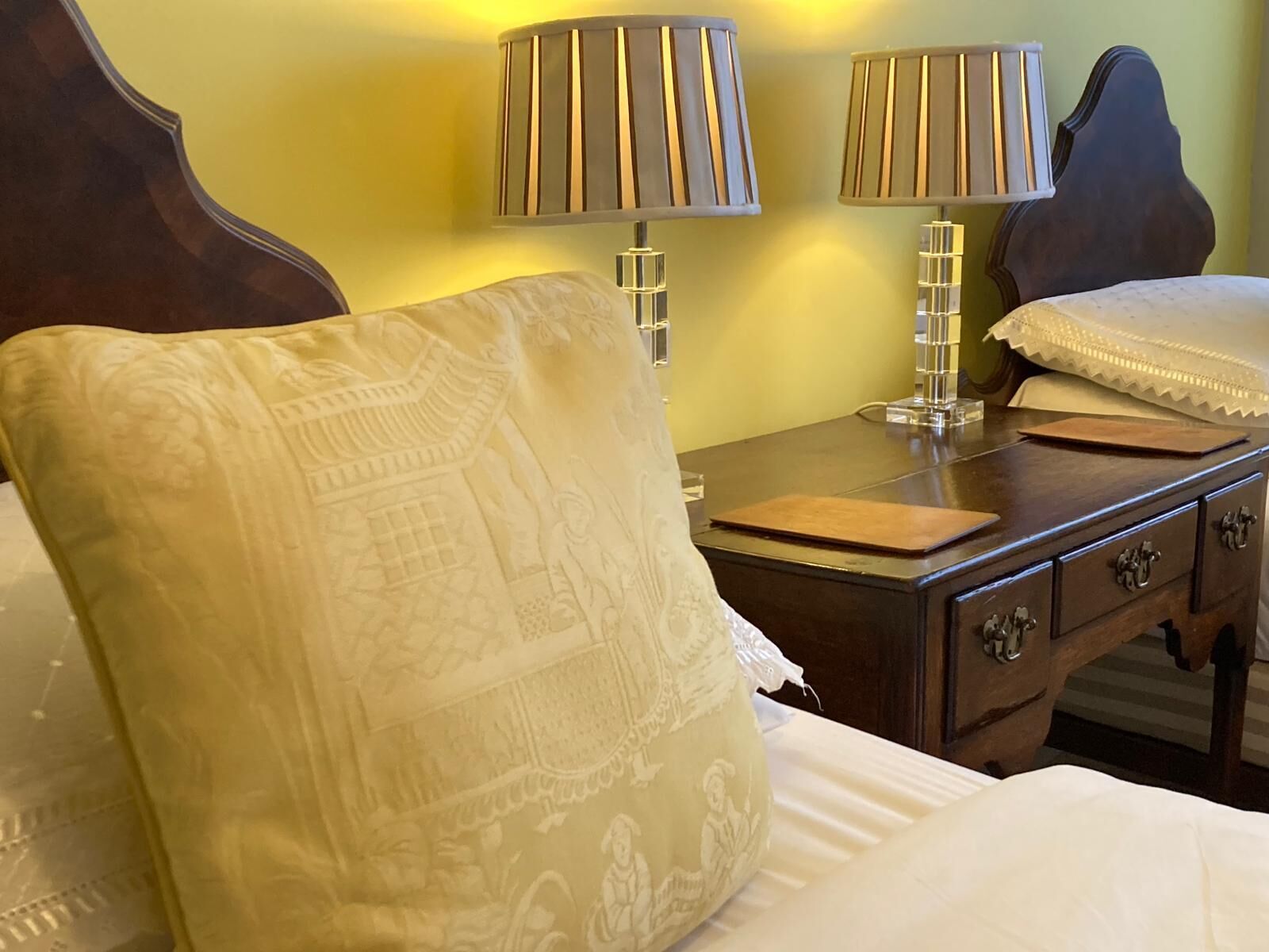 A hotel room with a bed, a nightstand with two lamps, a wooden headboard, and a decorative pillow.