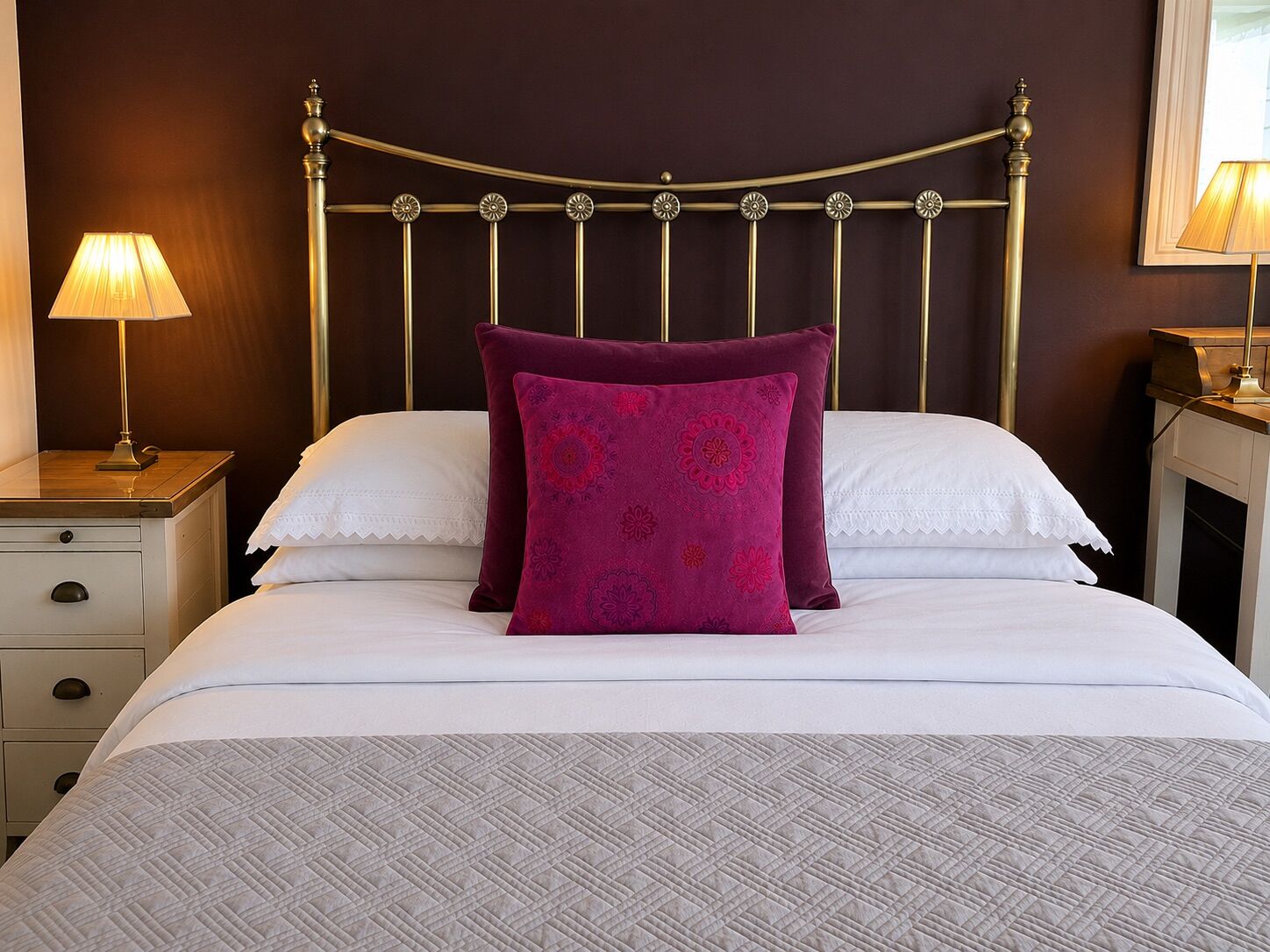 Un lit bien fait, avec une couvre-lit à motifs, deux oreillers, une table de chevet avec une lampe et un miroir fixé au mur.