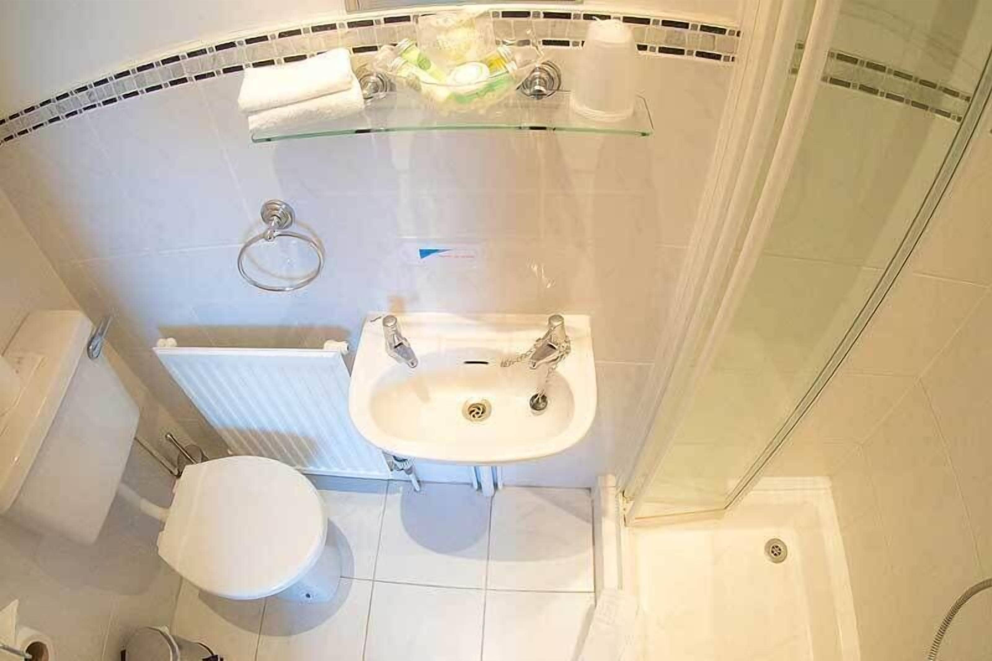 A bathroom with a glass shelf, a white sink, a toilet, and a shower area.