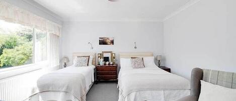 A bedroom with two beds, a dresser, a mirror, and a window with a view of greenery.