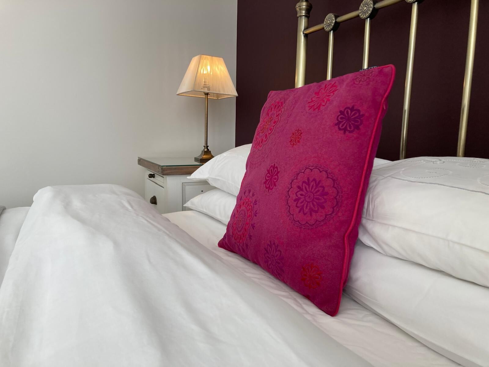 A neatly made bed with white linens and a single pink pillow with floral patterns.