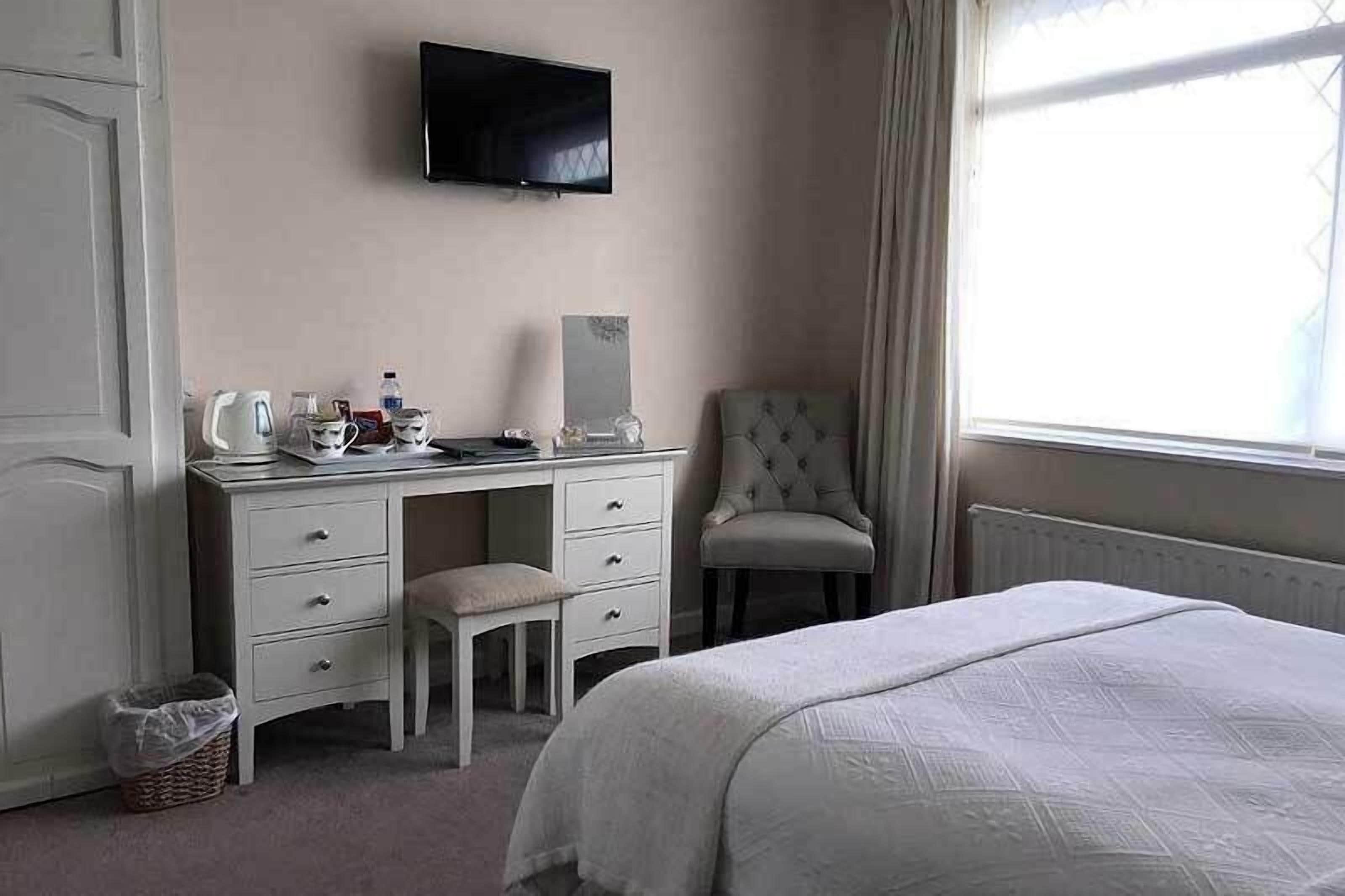 A bedroom with a bed, a desk with a chair, a television, and a window with curtains.
