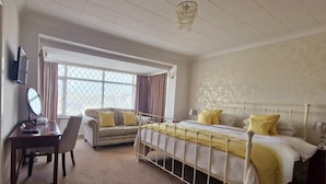 A bedroom with a bed, a desk, a chair, a sofa, and a large window. - The Coastyard (Chichester)