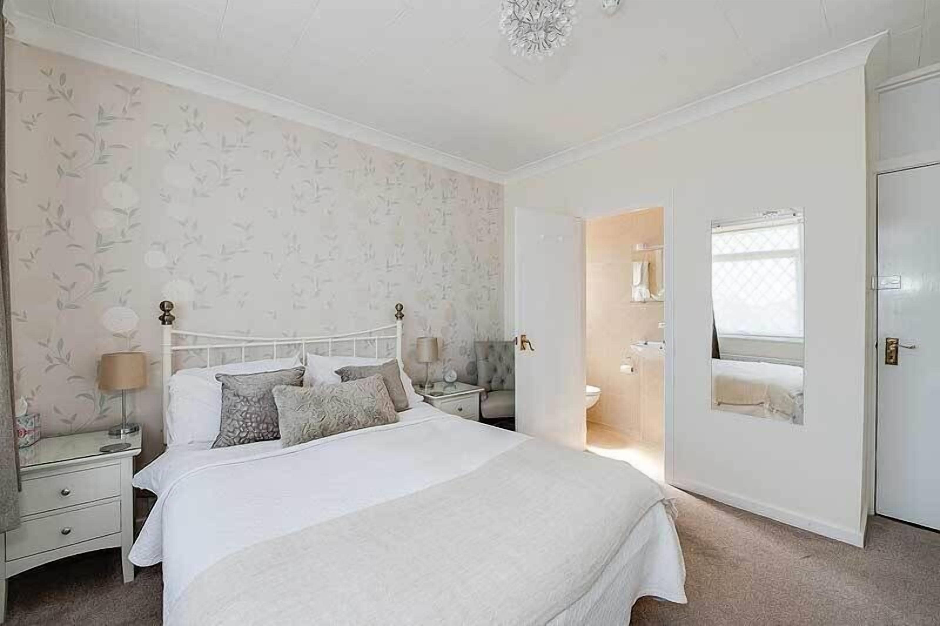 A bedroom with a large bed, two bedside tables, a nightstand, a mirror, and a door leading to a bathroom.