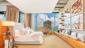 Une chambre d’hôtel moderne dotée d’un grand lit, d’un bureau et offrant une vue sur le paysage urbain grâce à de grandes fenêtres du sol au plafond.