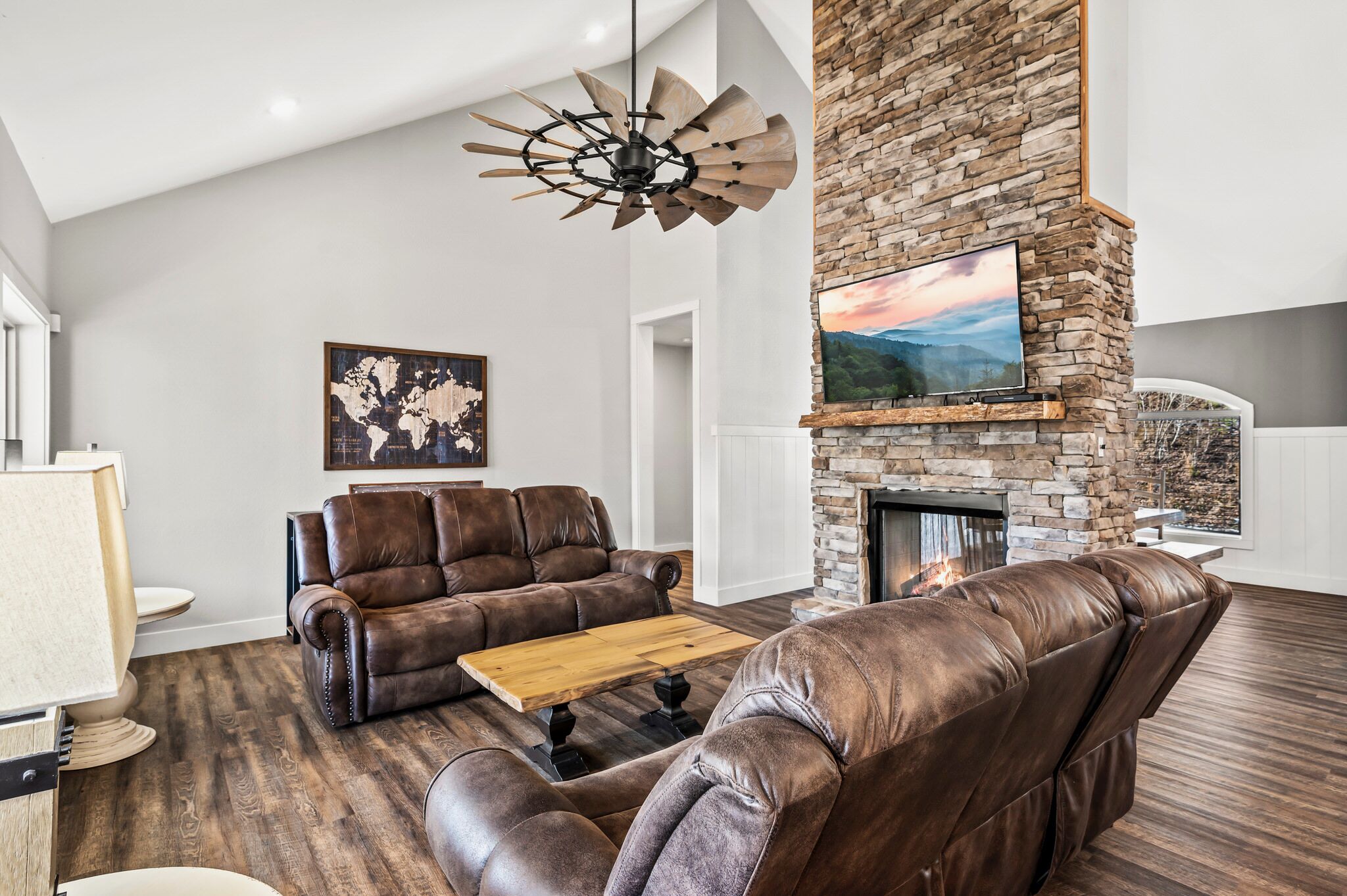 A modern living room with leather sofas, a wooden coffee table, a stone fireplace, and a world map artwork.