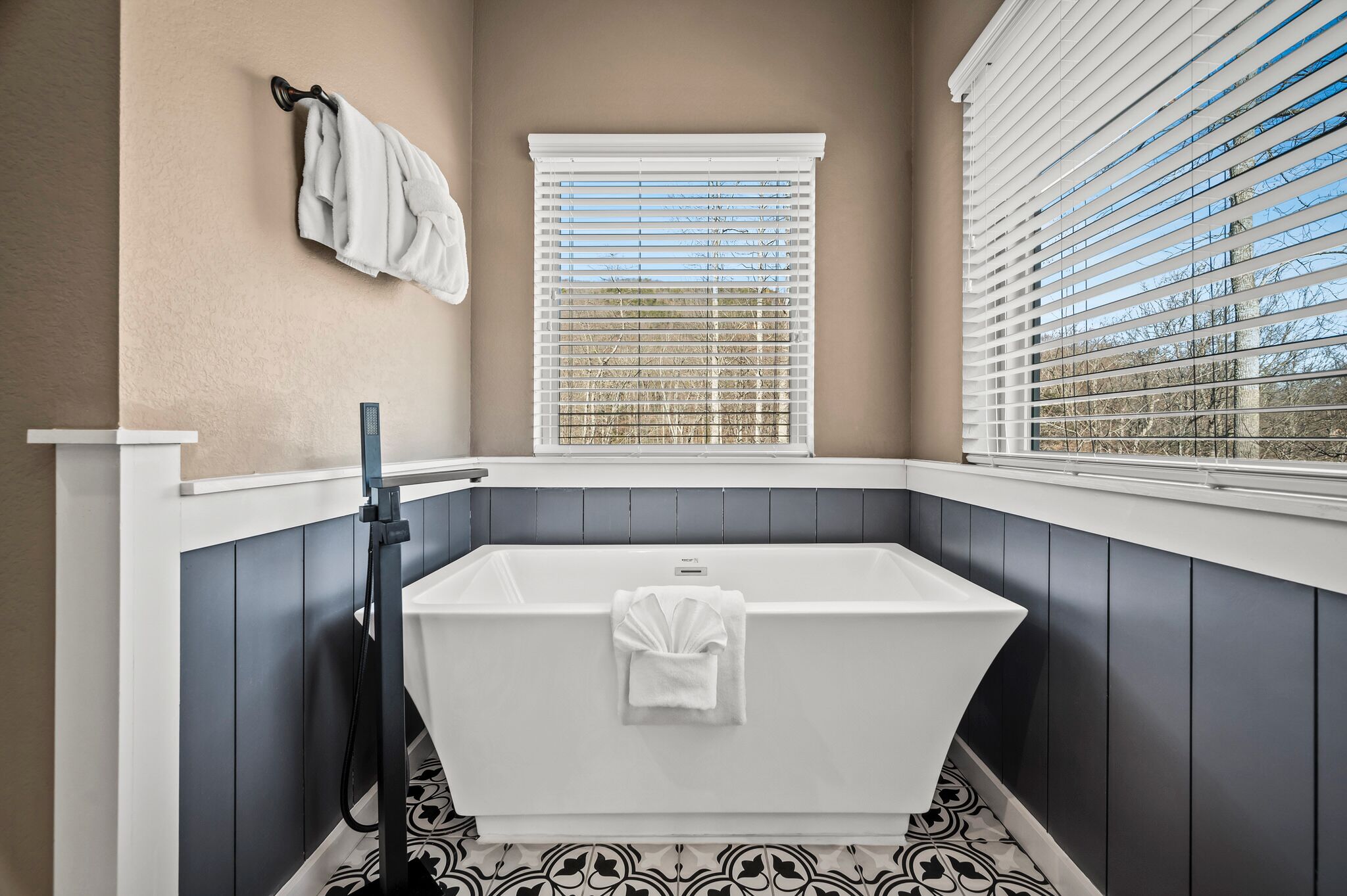 A modern bathroom with a freestanding bathtub, a window with blinds, and a towel rack.