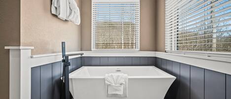 A modern bathroom with a freestanding bathtub, a window with blinds, and a towel rack.
