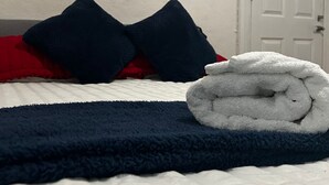 A neatly made bed with a folded white towel, two dark blue pillows, and a red blanket. A colorful abstract painting hangs on the wall above the bed. - Balham Double Deluxe Room 2 (London)