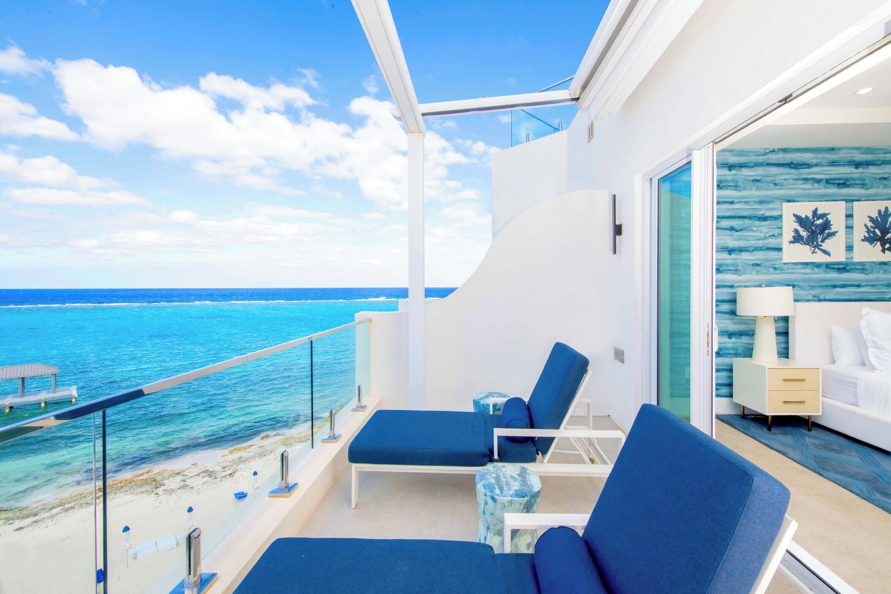 A balcony with a view of the ocean, a bed, and a nightstand.