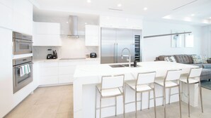 A modern kitchen with white cabinetry, stainless steel appliances, and a central island with bar stools. - Rum Point Resort #305 by Grand Cayman Villas (Seven Mile Beach)
