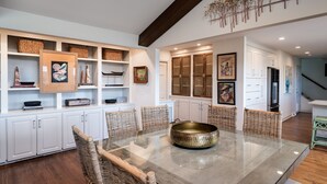 A dining area with a glass-top table, wicker chairs, white cabinetry, and decorative items on shelves.